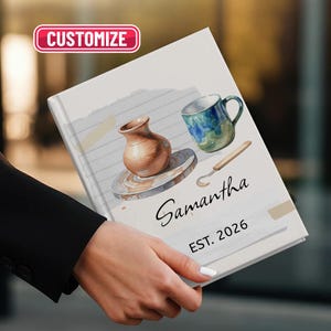 Może przedstawiać: Spersonalizowany notatnik z akwarelową ilustracją narzędzi garncarskich i kubka. Okładka notatnika przedstawia brązowy wazon, niebiesko-zielony kubek oraz imię "Samantha" z rokiem "EST. 2026". Słowo "DOSTOSUJ" znajduje się w różowym prostokącie.