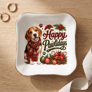 May include: A square white ceramic trinket dish with gold trim featuring a beagle wearing a red and green plaid scarf. The design includes a Santa hat, Christmas ornaments, a gift box, and the text Happy Pawlidays in red and green script.
