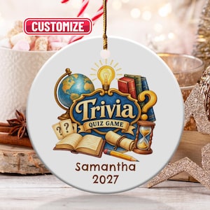May include: A round white ceramic ornament featuring a colourful illustration of a globe, books, a lightbulb, an hourglass, and a pencil. The text reads "Trivia Quiz Game" with "Samantha" and "2027" printed below. A red "CUSTOMIZE" label is at the top.