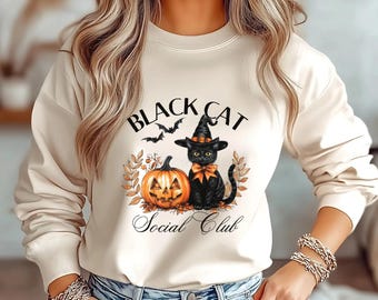 May include: Cream-colored sweatshirt featuring a Halloween-themed graphic. The design includes a black cat wearing a witch hat, a carved pumpkin, and the text "Black Cat Social Club" with bats. The cat has an orange bow.