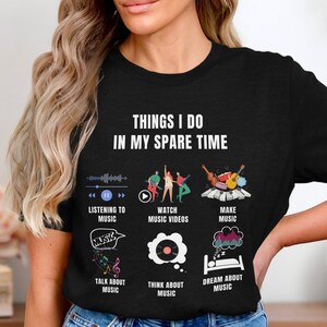 Op de afbeelding: Zwart T-shirt met de tekst "THINGS I DO IN MY SPARE TIME" en illustraties van muziekgerelateerde activiteiten. De illustraties omvatten naar muziek luisteren, muziekvideo's bekijken, muziek maken en over muziek dromen.