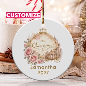 Peut inclure: Une décoration ronde en céramique blanche suspendue par un cordon doré. Le centre présente un cadre doré orné avec le texte Quinceañera, un carrosse, un château et des roses roses. Sous le cadre, le texte Samantha 2027 est imprimé en lettres dorées.