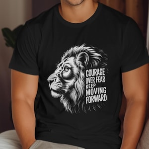 Pode incluir: Camiseta preta com um desenho detalhado da cabeça de um leão branco e o texto "COURAGE OVER FEAR KEEP MOVING FORWARD". A camiseta é de gola redonda.