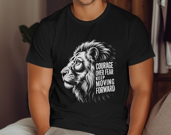 Op de afbeelding: Zwart T-shirt met een gedetailleerde witte leeuwenkopafbeelding. De afbeelding bevat de tekst "COURAGE OVER FEAR KEEP MOVING FORWARD" in het wit. Het shirt heeft een ronde hals.
