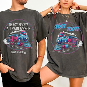 May include: Two charcoal gray t-shirts with a colorful train graphic. One shirt reads "I'M NOT ALWAYS A TRAIN WRECK, Just kidding." The other says "TOOT TOOT!" The train is blue, pink, and red.