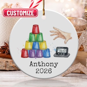 May include: A white ceramic ornament with a colorful illustration of stacked cups, a hand, and a timer. The text "Anthony 2026" is printed below the illustration. The word "Customize" is in a red box at the top.