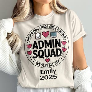 May include: Cream-colored t-shirt with a circular graphic that reads "ADMIN SQUAD" in bold black letters, surrounded by hearts and the text "ORGANIZING CHAOS SINCE FOREVER" and "WE SLAY ALL DAY". Below is the name "Emily" and the year "2025".