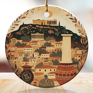May include: Round ceramic ornament featuring a stylized illustration of an ancient Greek city with buildings, columns, and pottery. The design includes a mountain with a temple, a sun, and decorative leaves. The ornament hangs from a gold string.