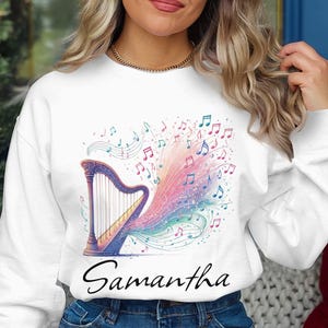 May include: White sweatshirt with a colorful harp and musical notes design. The text "Samantha" is printed below the design.