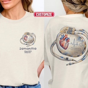 Pode incluir: Uma t-shirt de cor creme com um gráfico de um coração humano e um pacemaker com cabos. A parte da frente apresenta o nome Samantha e o ano 2027. A parte de trás mostra uma versão maior do mesmo gráfico com o texto PACEMAKER.