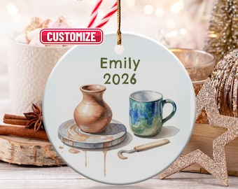 Può includere: Ornamento rotondo in ceramica con un design ad acquerello a tema ceramica. Presenta un vaso marrone, una tazza blu e verde e una ruota da vasaio. L'ornamento è iscritto con il nome "Emily" e l'anno "2026".