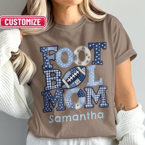 Puede incluir: Una camiseta de manga corta color canela con un gráfico que incluye el texto FOOTBALL MOM y el nombre Samantha. Las letras están rellenas con varios patrones azules y blancos, incluyendo cuadros vichy, estrellas y flores. Incluye un gráfico de fútbol.