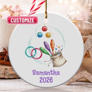 May include: A white ceramic ornament with a colorful illustration of juggling equipment, including clubs, rings, and balls. The word "CUSTOMIZE" is in a red box at the top. The name "Samantha" and the year "2026" are printed in purple.
