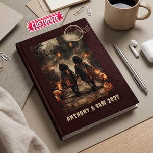 May include: A dark maroon hardcover journal featuring a rectangular illustration of two children walking toward a haunted house at night, surrounded by glowing jack-o'-lanterns. The text "ANTHONY & SAM 2027" is printed in a light color at the bottom.