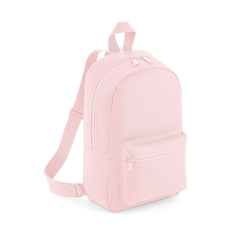 Puede incluir: Una mochila de lona rosa claro con un bolsillo frontal con cremallera y correas ajustables.
