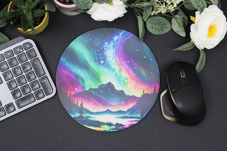 Pu&ograve; includere: Tappetino per mouse rotondo con una scena colorata di aurora boreale sopra una catena montuosa e un lago. L'aurora &egrave; in tonalit&agrave; di rosa, viola, verde e blu. La catena montuosa &egrave; blu scuro e il lago &egrave; blu chiaro. Lo sfondo &egrave; un cielo blu scuro con stelle.