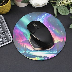 Pu&ograve; includere: Un mouse wireless nero con un accento dorato si trova su un tappetino per mouse rotondo con un design colorato di aurora boreale. Il tappetino per mouse presenta un lago blu scuro con una foresta sullo sfondo.