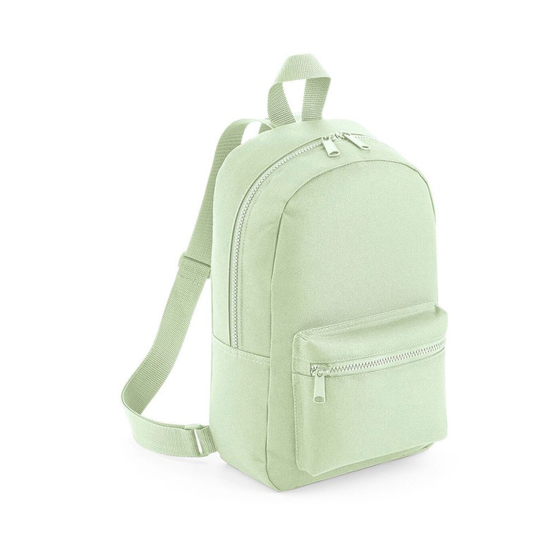 Puede incluir: Una mochila de lona verde claro con un bolsillo frontal con cremallera y correas ajustables.