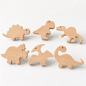 May include: A set of six light-colored wooden dinosaur-shaped cutouts, each featuring a small circular hole near the top. The collection includes various species such as a stegosaurus, a tyrannosaurus, and a long-necked sauropod, all with a smooth, natural wood grain finish.