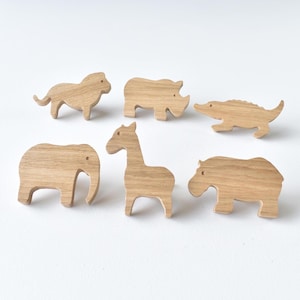 May include: A set of six light brown wooden animal figures featuring a lion, a rhinoceros, a crocodile, an elephant, a giraffe, and a hippopotamus. Each animal is carved from wood with a visible grain pattern and simple, smooth outlines.