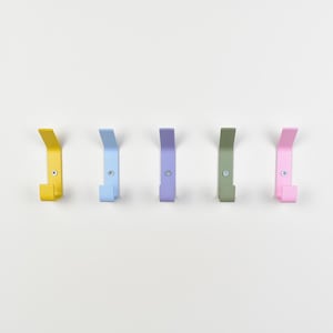 May include: A set of five wall-mounted metal hooks arranged in a horizontal row. Each hook features a distinct matte color: yellow, light blue, lavender, sage green, and pink. Every hook is secured to the wall with a single visible silver screw.