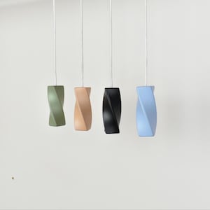 Op de afbeelding: Vier decoratieve lichtschakelaars in olijfgroen, beige, zwart en lichtblauw. Elke trekker heeft een gedraaid, cilindrisch ontwerp en hangt aan een wit koord. De trekkers hangen tegen een effen witte achtergrond, wat hun unieke vormen en kleuren benadrukt.