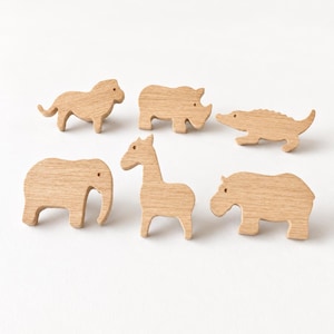 May include: A set of six light brown wooden animal figures including a lion, rhinoceros, crocodile, elephant, giraffe, and hippopotamus. Each figure is carved from smooth, light-colored wood with a natural grain and simple, flat-cut silhouettes.