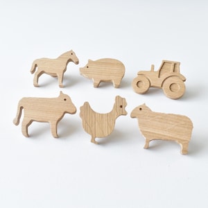 Op de afbeelding: Een set van zes lichtbruine houten uitsparingen in de vorm van een paard, een varken, een tractor, een koe, een kip en een schaap. Elk stuk heeft een gladde afwerking met een natuurlijke houtnerf en duidelijke silhouetten van boerderijdieren.