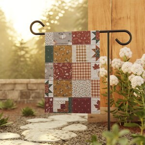 Puede incluir: Una bandera de jardín rectangular con un diseño de patchwork que incluye varios patrones de temática otoñal, como calabazas, hojas de arce, estampados florales y cuadros vichy en tonos amarillo mostaza, naranja, verde bosque y crema.