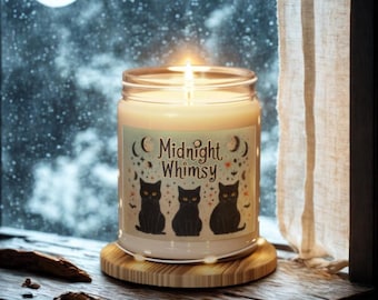 Może przedstawiać: Zapalone świeca w szklanym słoiku z etykietą "Midnight Whimsy". Etykieta przedstawia trzy ilustracje czarnych kotów z pomarańczowymi oczami, nietoperzami i gwiazdami. Świeca stoi na drewnianej podstawce, a w tle widać zaśnieżone okno.