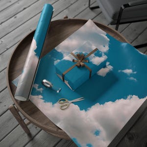 May include: A blue gift box with a brown ribbon and bow is wrapped in blue and white wrapping paper with a cloud pattern. The wrapping paper is rolled up next to the gift box.