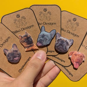 May include: A set of six dog breed pins featuring a French Bulldog, a Pug, a Brussels Griffon, a Dachshund, a Jack Russell Terrier, and a Pitbull. The pins are on brown cards with the text "Bijiko Designs" printed on them.