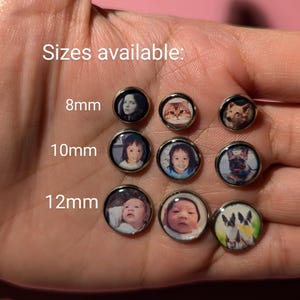 May include: A close-up of a hand holding various sizes of round photo earrings. The earrings are available in 8mm, 10mm, and 12mm sizes. The photos on the earrings include a cat, a dog, and a baby.