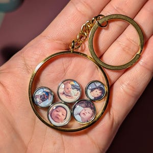 Könnte beinhalten: Goldener Schlüsselanhänger mit einem runden Rahmen, der fünf kleine runde Fotoeinsätze enthält. Die Fotos sind von Babys und Kleinkindern.