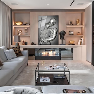 May include: A modern living room interior with a gray sofa, a glass coffee table, and a fireplace. A large framed artwork of a silver couple embracing hangs above the fireplace. The text "GlasState Luxury" is visible on the fireplace.