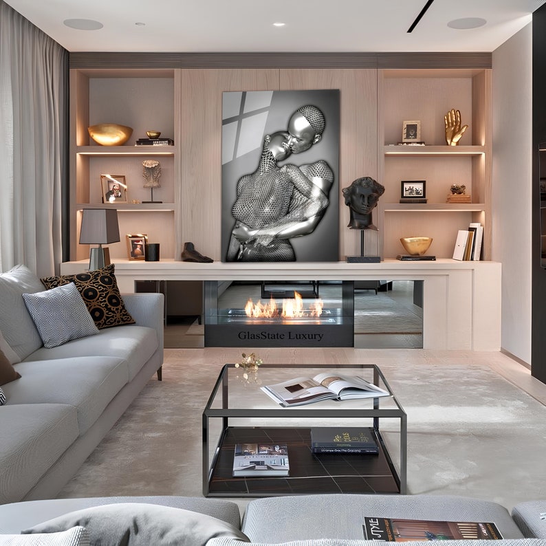 May include: A modern living room interior with a gray sofa, a glass coffee table, and a fireplace. A large framed artwork of a silver couple embracing hangs above the fireplace. The text "GlasState Luxury" is visible on the fireplace.