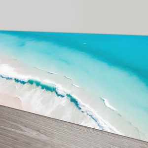 May include: An aerial view of a turquoise ocean with white foamy waves crashing on a sandy beach.
