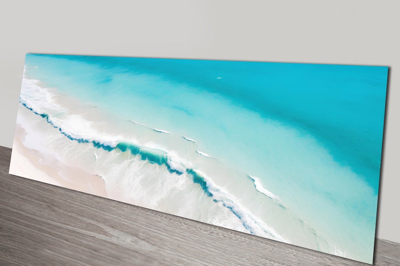 May include: An aerial view of a turquoise ocean with white foamy waves crashing on a sandy beach.
