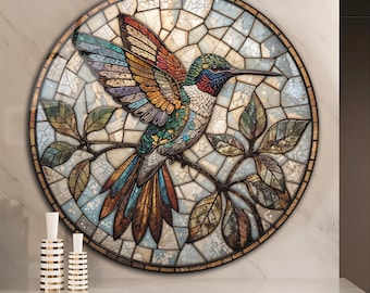 May include: A round, stained-glass-style wall art piece featuring a colorful hummingbird with outstretched wings. The bird is perched on a branch with leaves, set against a mosaic background. The artwork has a gold-toned frame and is displayed on a white wall.