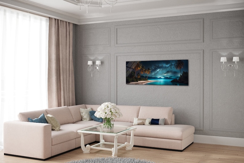May include: A panoramic photograph of a tropical beach at night with palm trees, a starry sky, and a glowing moon reflecting on the water. The image is framed and hanging on a grey wall in a living room with a white sectional sofa and a white coffee table.