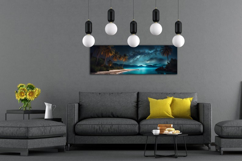 May include: A living room interior with a grey sofa and two yellow throw cushions. A black coffee table with a cup and saucer and a plate of pastries sits in front of the sofa. A grey ottoman sits to the right of the sofa. A black metal tray with a vase of yellow sunflowers sits on a black metal side table to the left of the sofa. A panoramic photograph of a tropical beach scene with palm trees and a starry sky hangs on the wall above the sofa. Six black and white pendant lights hang from the ceiling.