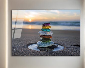 Puede incluir: Impresión enmarcada de una pila de piedras lisas y coloridas en una playa de arena al atardecer. Las piedras son de color púrpura, amarillo, turquesa, blanco, naranja y verde. El océano y el sol están en el fondo.