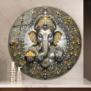 May include: A circular wall art piece featuring a detailed silver and gold Ganesha figure holding a bowl of yellow sweets. The deity is surrounded by an intricate mandala pattern adorned with embedded clear, green, and amber-colored gems.