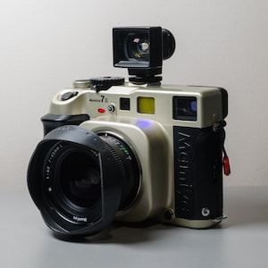 May include: A silver and black Mamiya 7 II medium format film camera with a 43mm lens and a flash attachment.