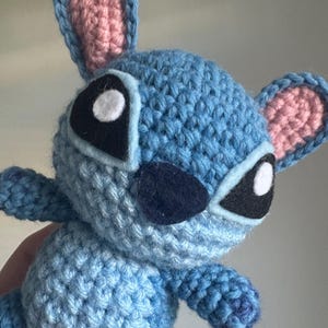 May include: A blue crocheted Stitch plush toy with pink ears, white eyes, and a black nose.