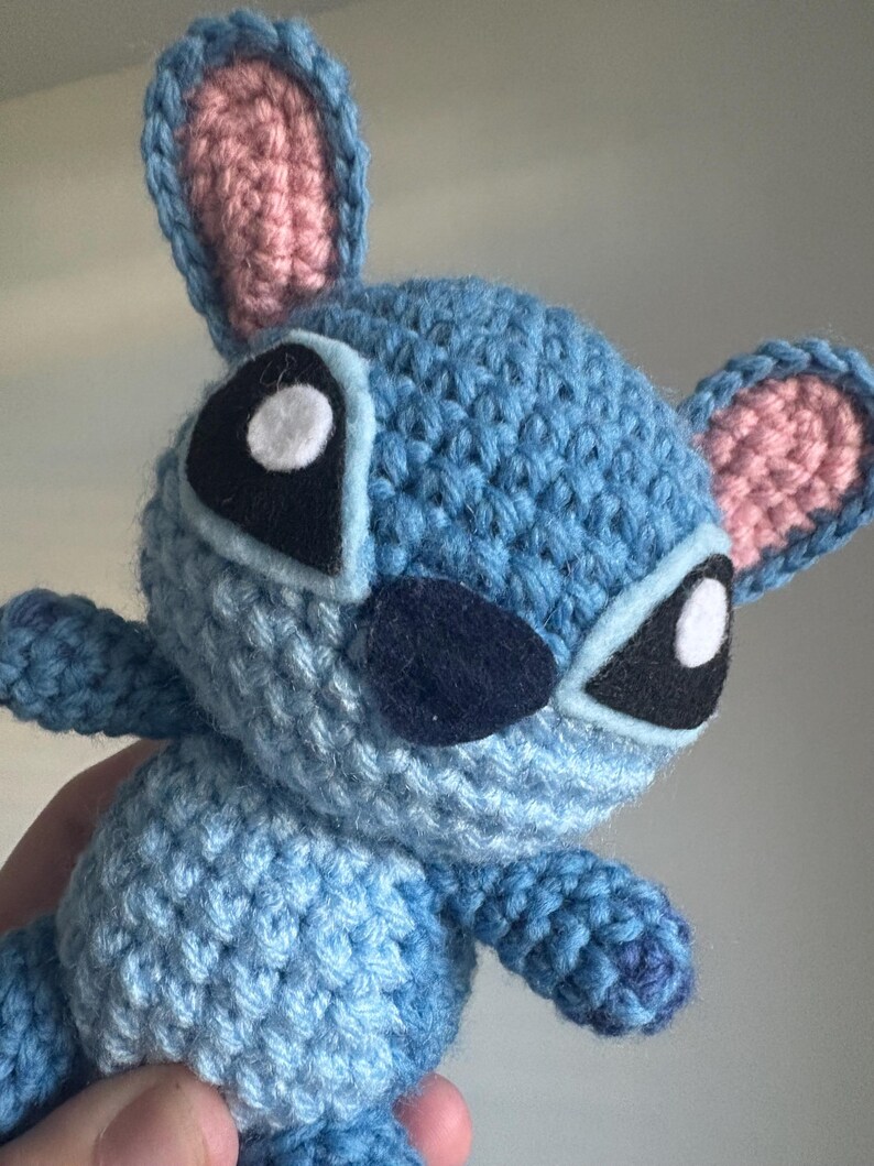 May include: A blue crocheted Stitch plush toy with pink ears, white eyes, and a black nose.
