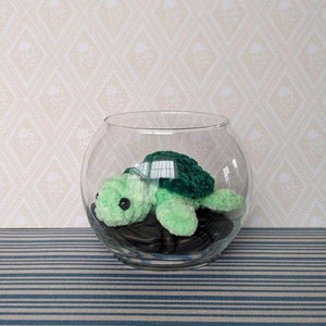 Peut inclure: Un jouet de tortue en crochet vert à l'intérieur d'un bol en verre transparent avec des cailloux noirs.