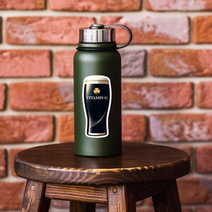 May include: A dark green water bottle with a silver cap and black handle. A sticker on the bottle features a black stout beer with white foam, a gold shamrock, and the words "VITAMIN G" in white.