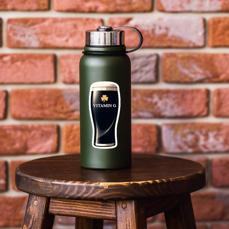 May include: A dark green water bottle with a silver cap and black handle. A sticker on the bottle features a black stout beer with white foam, a gold shamrock, and the words "VITAMIN G" in white.