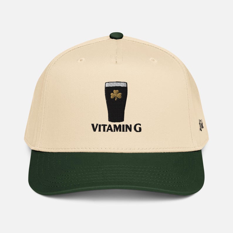 May include: Cream-colored baseball cap with a dark green brim and a black top button. The cap features an embroidered image of a pint of stout with a gold shamrock and the text "VITAMIN G" in black.